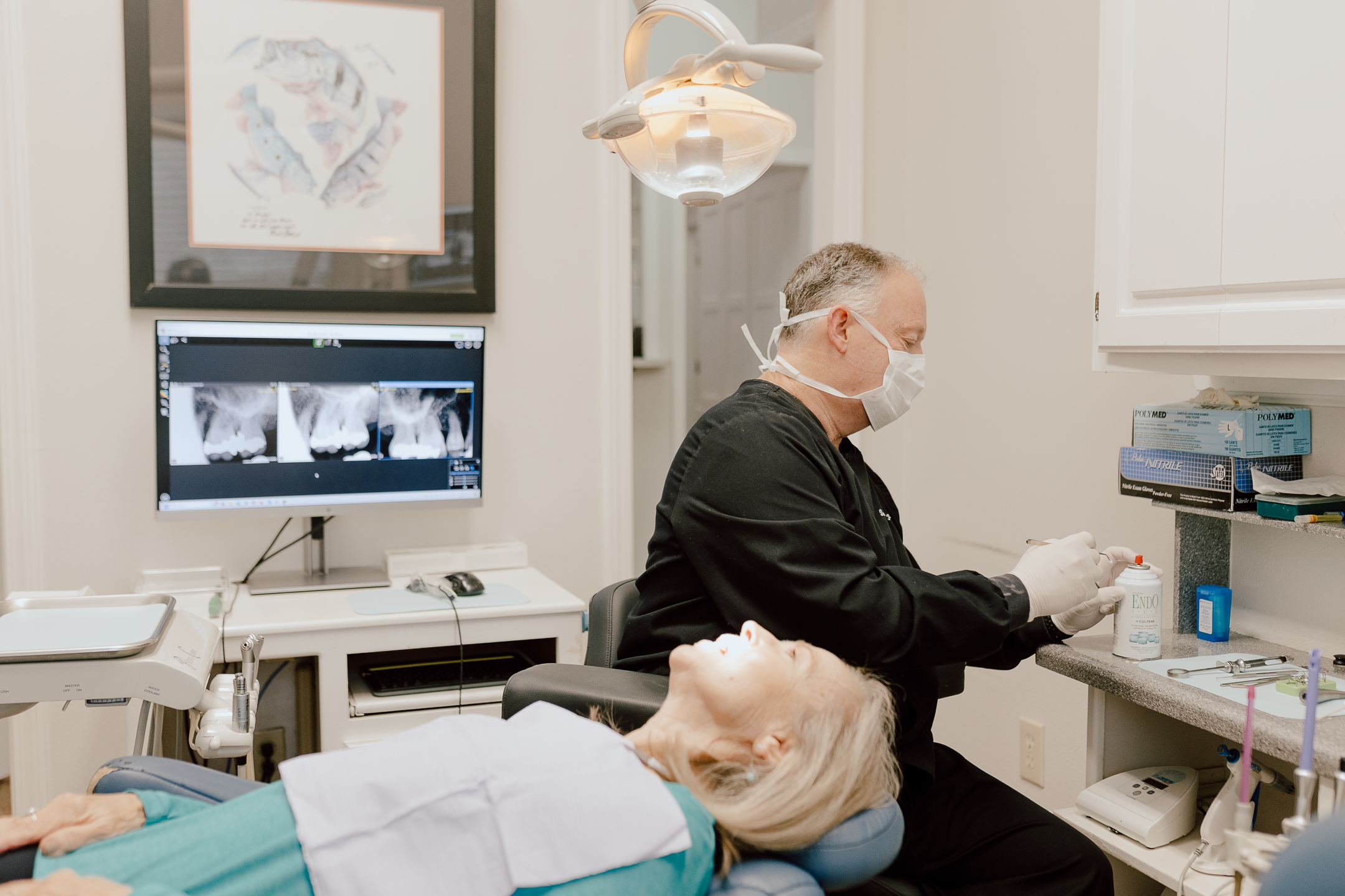 Dentist in mask and gloves preparing dental tools near a patient who came for dental emergency, lying in a dental chair.