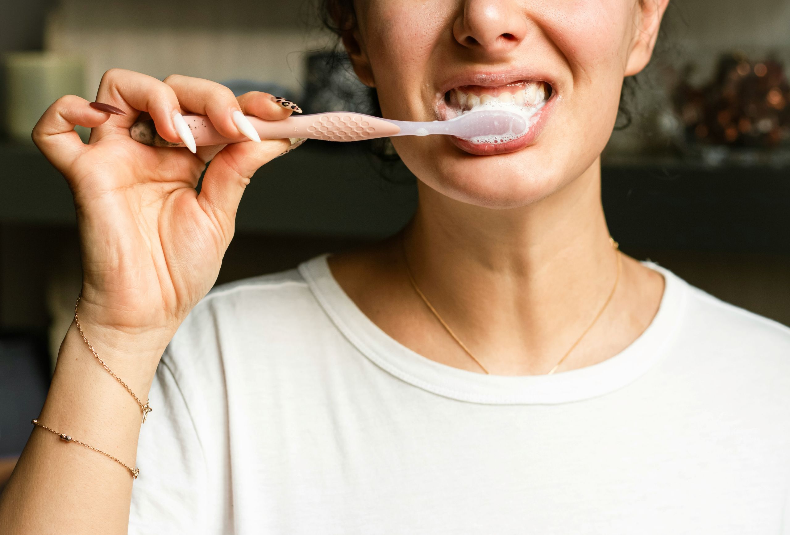 A person wearing a white shirt is brushing their teeth with a pink toothbrush, possibly after an endodontic retreatment. Only the lower half of their face and one hand are visible.