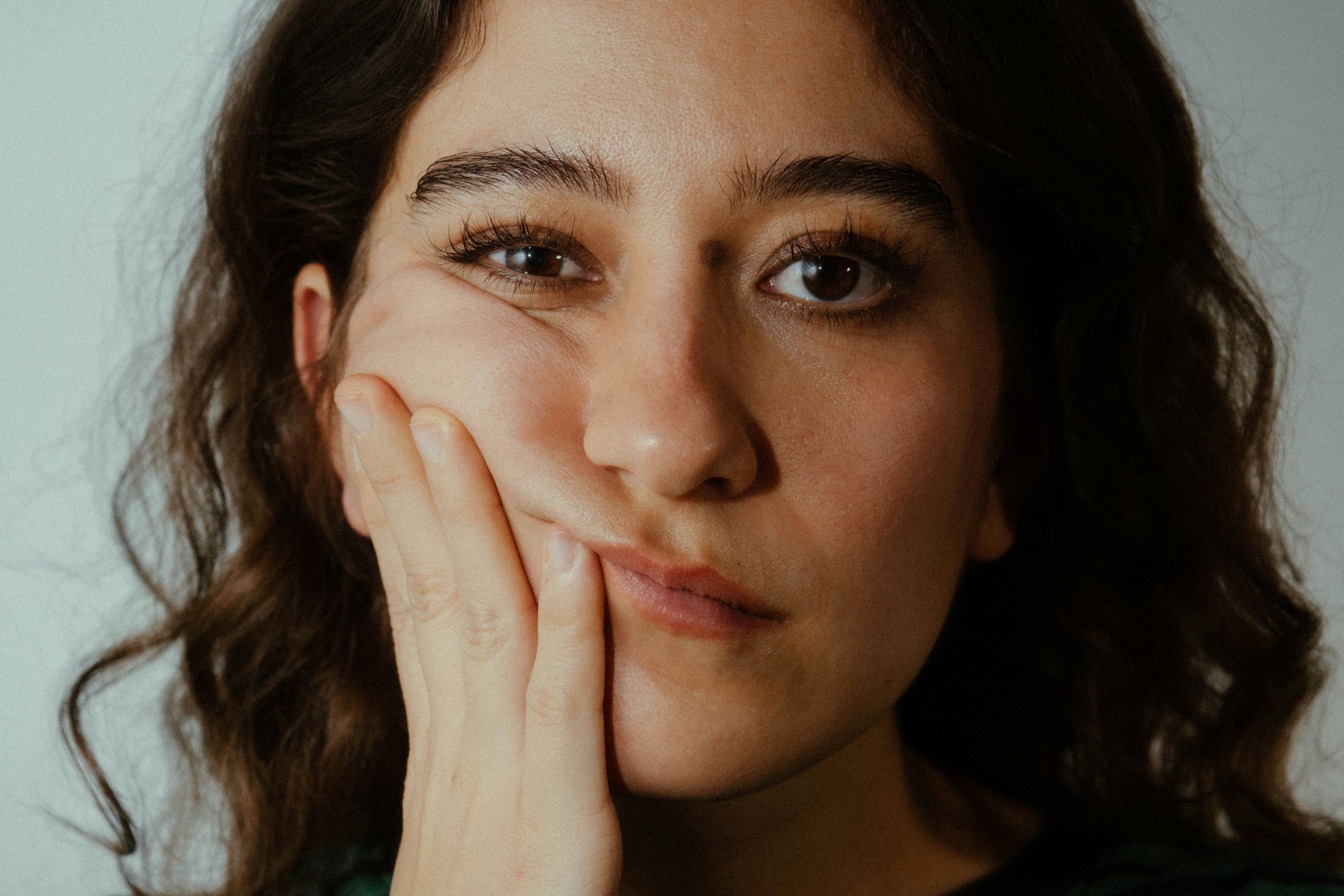 A young woman looking at the camera with her hand resting against her cheek.
